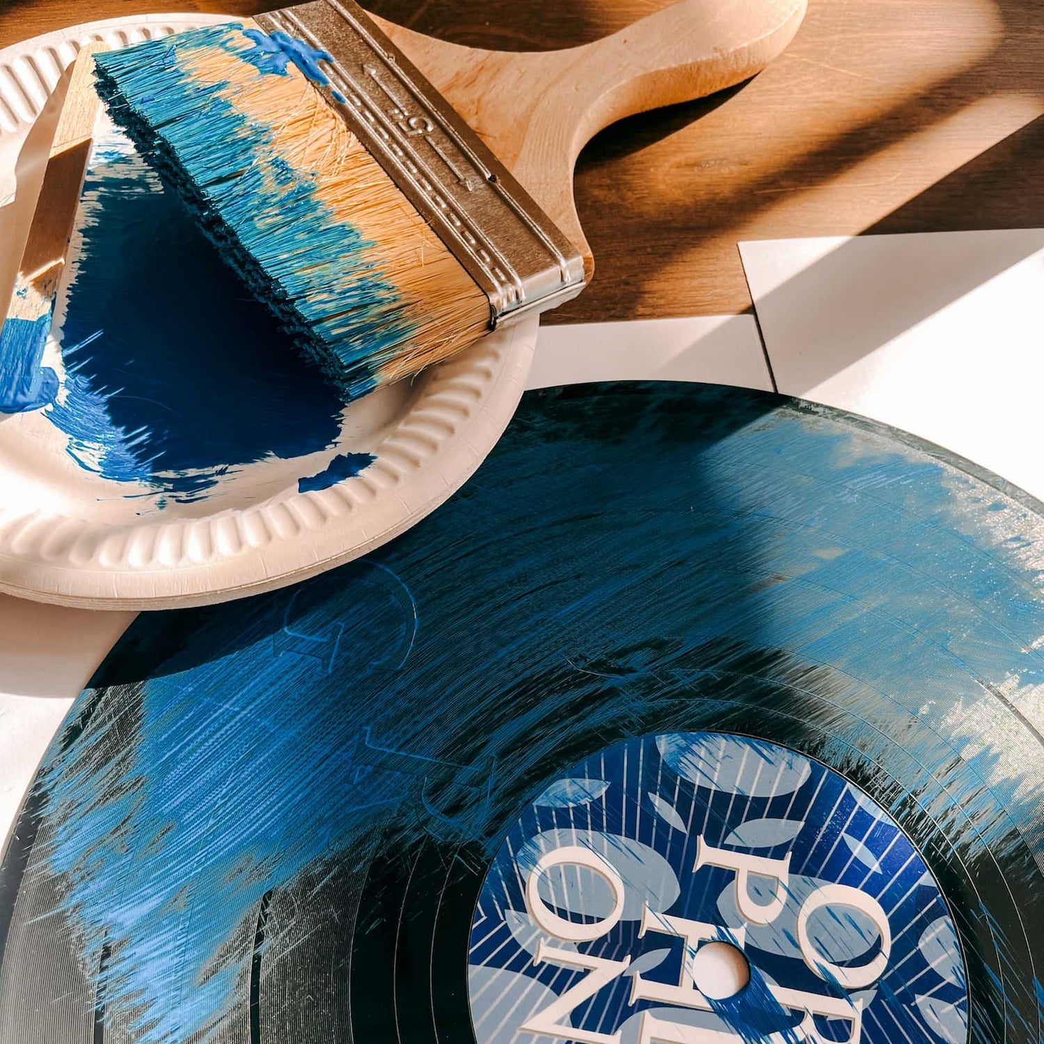 Pinsel mit blauer Farbe neben Schallplatte mit blauen Streifen beim Vinylplatten bemalen Workshop von GRIMMS GARTEN, DIY Kreativkurs in Berlin
