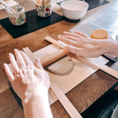 Zwei Hände rollen weichen Ton gleichmäßig auf weißer Platte aus – Vorbereitung Handformen Ton im Töpferkurs Englisch