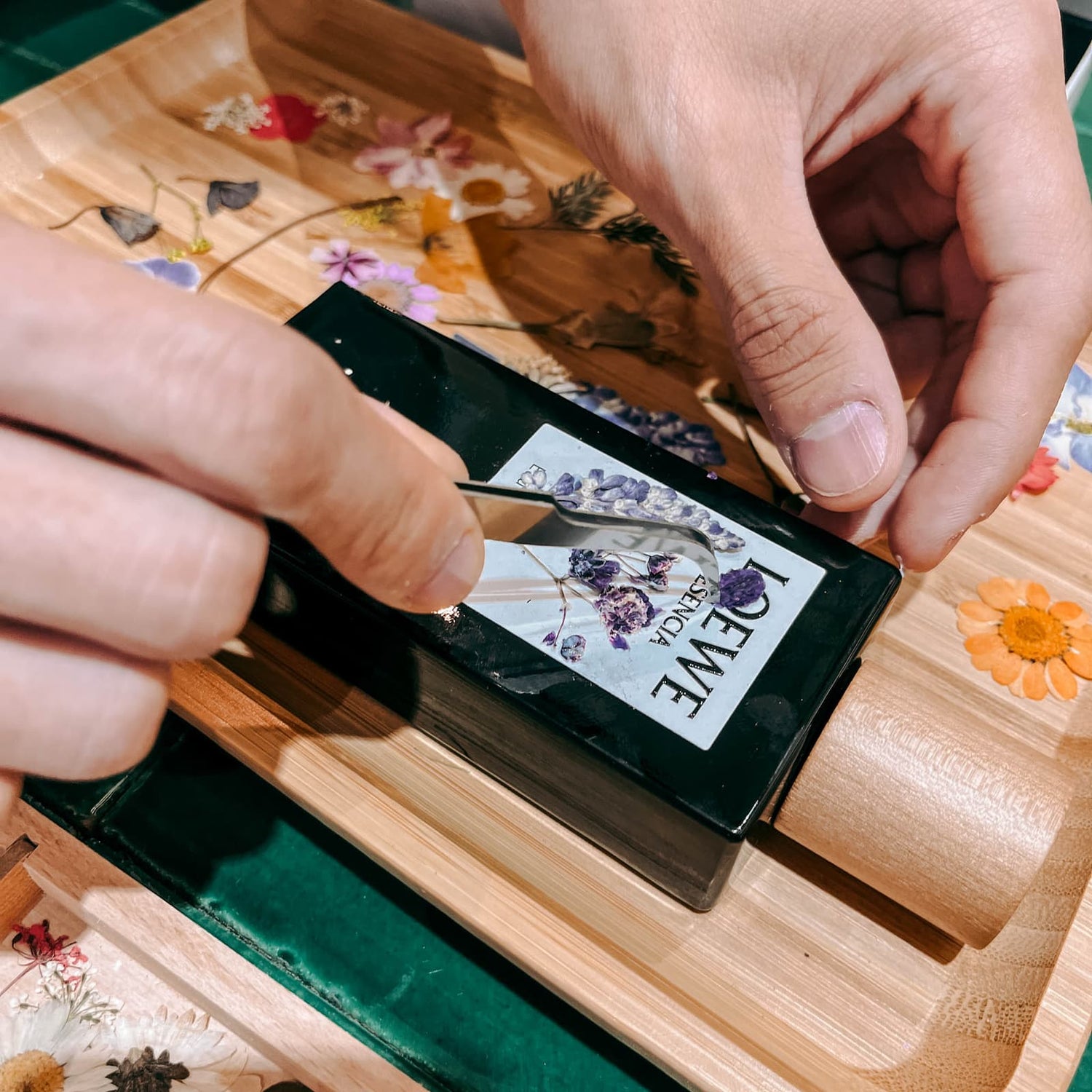 Hand klebt Trockenblumen auf Parfum Flakon im kreativen DIY Workshop von GRIMMS GARTEN in Berlin