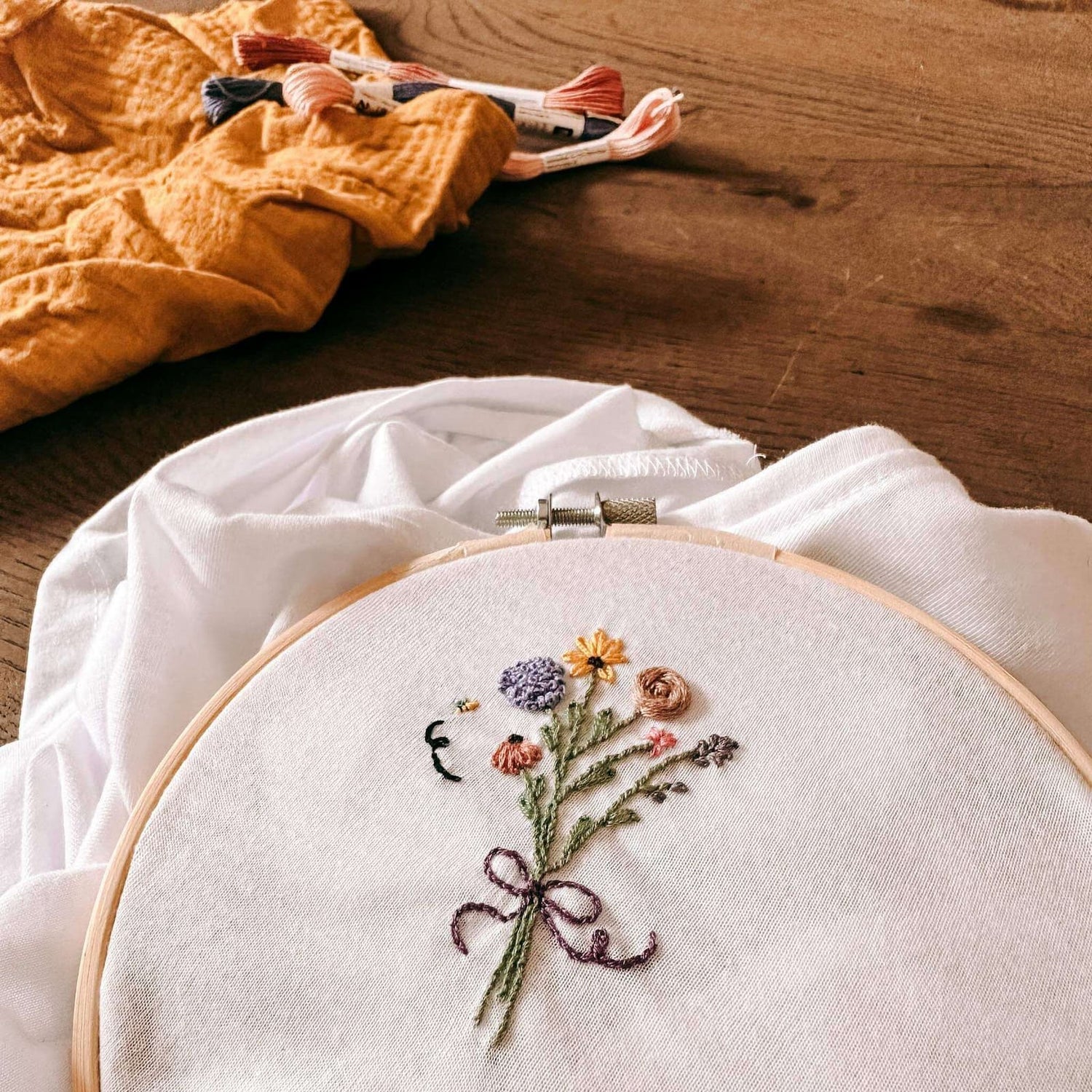 Stickrahmen mit T-Shirt und Blumenmotiv, Garn im Hintergrund – stickkurs berlin, embroidery workshop, kleidung besticken.