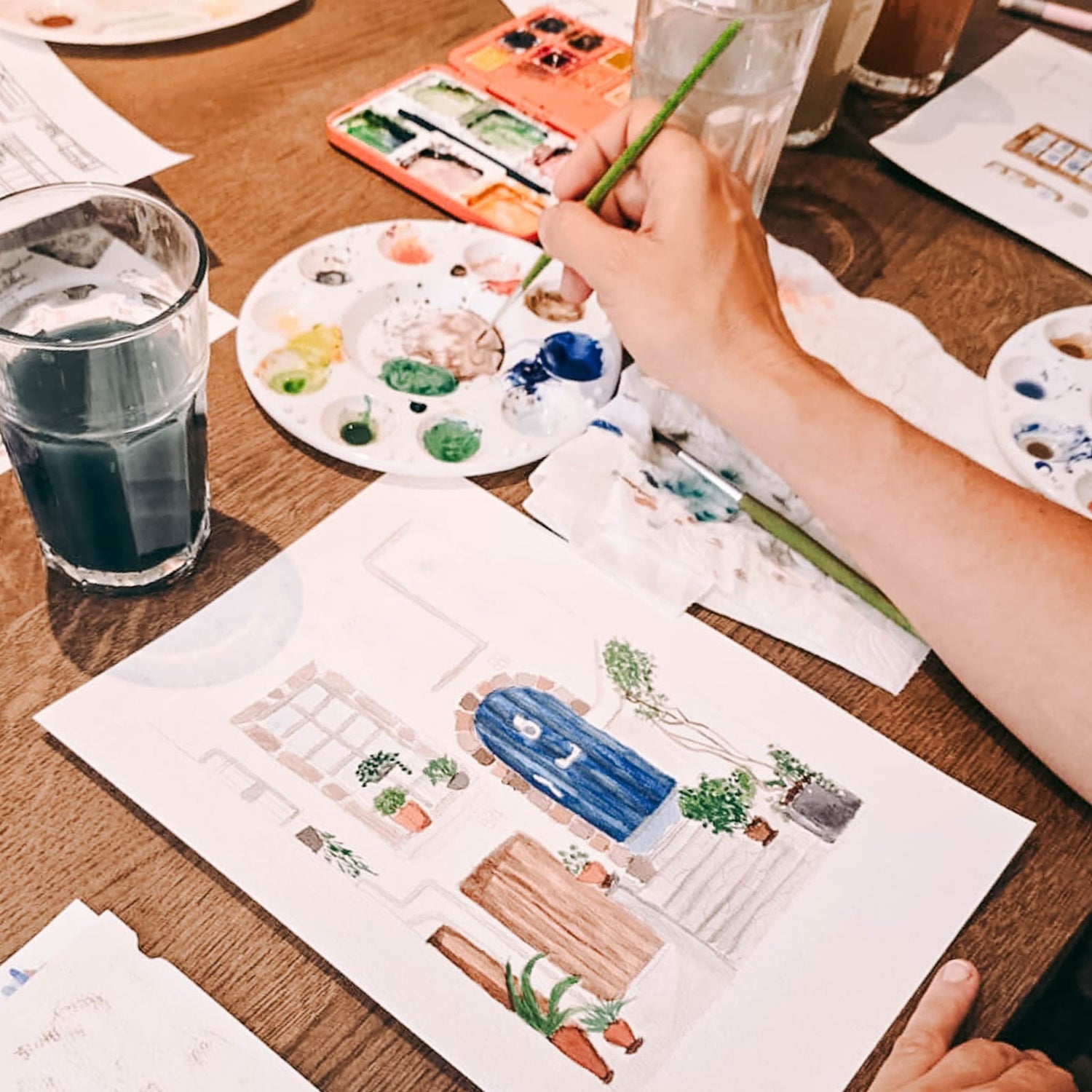 Hände malen mit blauer Aquarellfarbe an einem Bild beim Aquarell Workshop von GRIMMS GARTEN Berlin